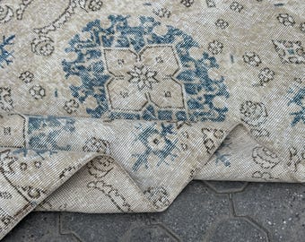 May include: A beige rug with a blue and white geometric pattern. The rug is folded in half and the pattern is visible on both sides.