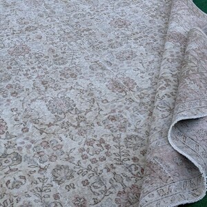 May include: A vintage rug with a floral pattern in shades of beige and brown. The rug is folded in half and has a worn, distressed look.