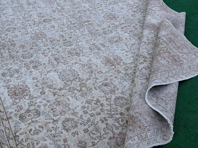 May include: A vintage rug with a floral pattern in shades of beige and brown. The rug is folded in half and has a worn, distressed look.