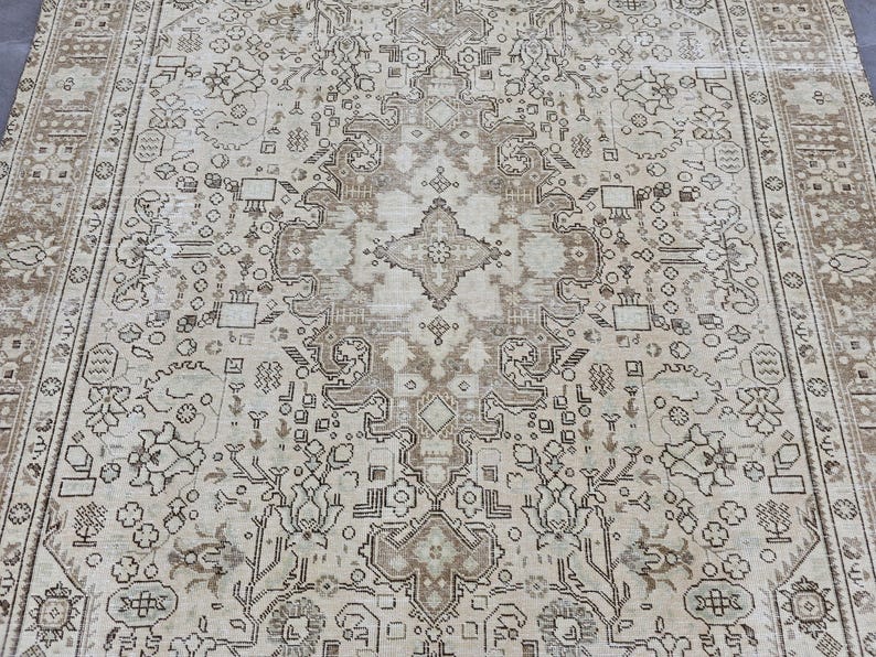K&ouml;nnte beinhalten: Ein Teppich im antiken Stil mit einem zentralen Medaillon-Design. Der Teppich hat einen cremefarbenen Hintergrund mit aufwendigen Mustern in Braun- und Beiget&ouml;nen. Der Rand hat ein detailliertes Blumendesign.