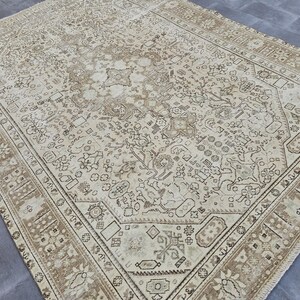 K&ouml;nnte beinhalten: Gro&szlig;er, rechteckiger beigefarbener Teppich mit einem komplizierten, sich wiederholenden Muster in Braun- und Cremet&ouml;nen. Der Teppich hat einen detaillierten Rand und ein zentrales Design mit floralen und geometrischen Elementen, die eine Vintage-&Auml;sthetik erzeugen.