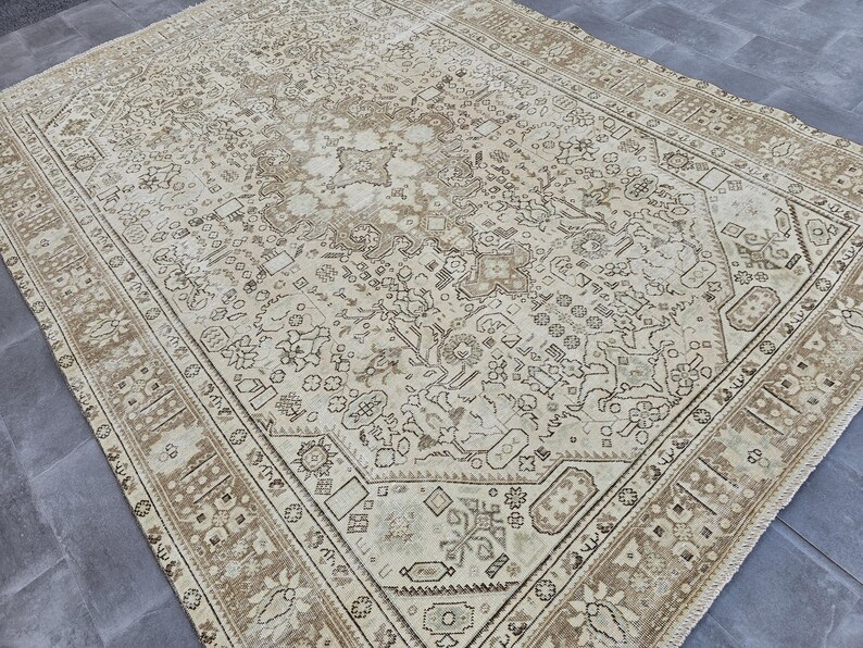 K&ouml;nnte beinhalten: Gro&szlig;er, rechteckiger beigefarbener Teppich mit einem komplizierten, sich wiederholenden Muster in Braun- und Cremet&ouml;nen. Der Teppich hat einen detaillierten Rand und ein zentrales Design mit floralen und geometrischen Elementen, die eine Vintage-&Auml;sthetik erzeugen.