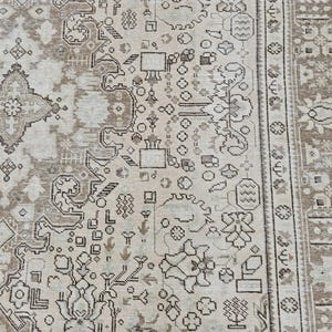 K&ouml;nnte beinhalten: Beige und braun gemusterter Teppich mit aufwendigem Design. Der Teppich hat ein zentrales Medaillon und einen Rand mit floralen und geometrischen Motiven. Die Farbpalette umfasst Beige, Braun und einen Hauch von Creme, was eine Vintage-&Auml;sthetik erzeugt.