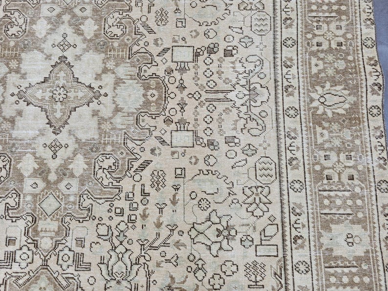 K&ouml;nnte beinhalten: Beige und braun gemusterter Teppich mit aufwendigem Design. Der Teppich hat ein zentrales Medaillon und einen Rand mit floralen und geometrischen Motiven. Die Farbpalette umfasst Beige, Braun und einen Hauch von Creme, was eine Vintage-&Auml;sthetik erzeugt.