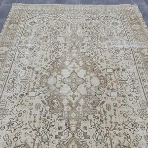 K&ouml;nnte beinhalten: Ein gro&szlig;er, rechteckiger Teppich mit einem aufwendigen, traditionellen Design. Der Teppich hat einen cremefarbenen Hintergrund mit einem detaillierten Muster in Braun- und Beiget&ouml;nen. Der Rand hat ein sich wiederholendes geometrisches Design.