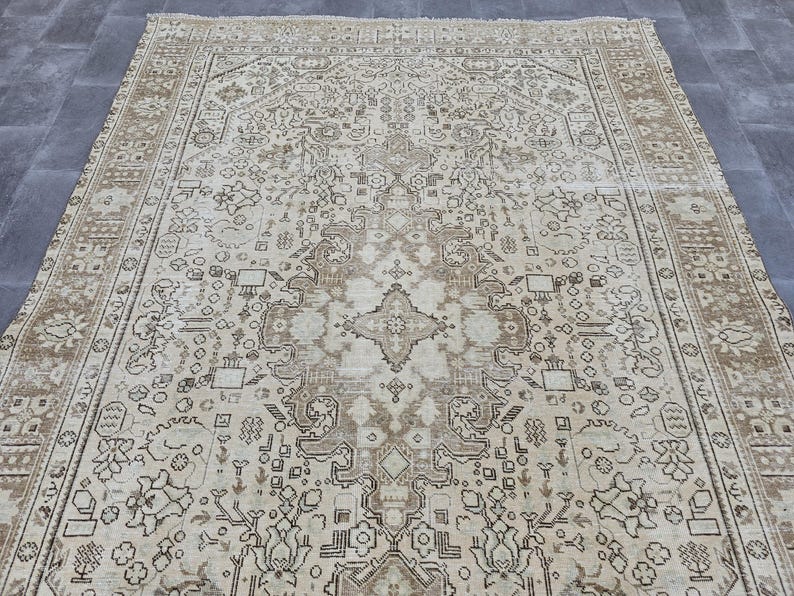K&ouml;nnte beinhalten: Ein gro&szlig;er, rechteckiger Teppich mit einem aufwendigen, traditionellen Design. Der Teppich hat einen cremefarbenen Hintergrund mit einem detaillierten Muster in Braun- und Beiget&ouml;nen. Der Rand hat ein sich wiederholendes geometrisches Design.