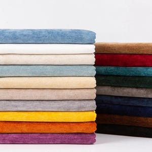 May include: A selection of fabric swatches in a range of colours, such as blue, cream, yellow, and purple. The fabric has a soft, textured appearance, possibly velvet or a similar material. The swatches are stacked neatly, showcasing the variety of shades.