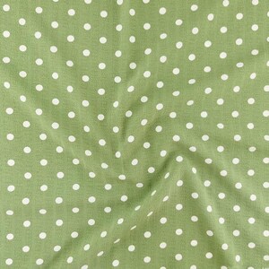 May include: A sage green fabric featuring a repeating pattern of small, evenly spaced white polka dots. The material has a subtle, crinkled texture with soft folds that create gentle shadows across the surface of the textile.