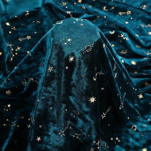 Op de afbeelding: Teal fluweelstof met een gouden sterrenbeeldpatroon. De stof is zacht en luxueus, perfect voor bekleding of knutselprojecten.