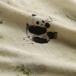 Pu&ograve; includere: Un tessuto color crema chiaro caratterizzato da un delicato motivo ricamato ripetuto di sottili foglie di bamb&ugrave; verdi. Una stampa grafica centrale raffigura un panda bianco e nero seduto mentre mangia, in un morbido stile a inchiostro.