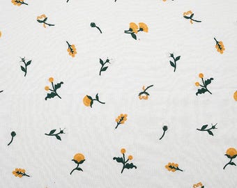 May include: A white fabric featuring a repeating pattern of small, embroidered yellow flowers with dark green stems and leaves. The floral motifs are scattered across the surface, showcasing detailed stitching in a consistent, delicate design.