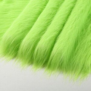 May include: A vibrant lime green faux fur fabric featuring long, dense synthetic fibers. The material is arranged in soft, cascading folds that create deep shadows and highlights, emphasizing the texture and bright, saturated color of the textile.