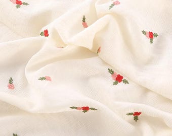May include: A piece of off-white fabric featuring a repeating pattern of small embroidered flowers. Each floral motif consists of a bright red bloom, a smaller light pink bud, and tiny green leaves, scattered across the textured, draped material.