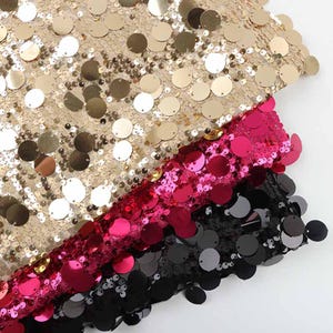 May include: Three layers of fabric covered in round, reflective sequins stacked on top of each other. The top layer is metallic gold, the middle layer is a vibrant hot pink, and the bottom layer is a solid matte black, all featuring circular discs.