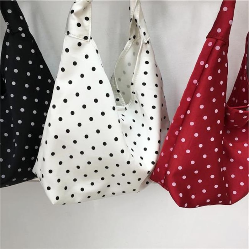 May include: Three fabric hobo bags with a knot handle design. One bag is black with white polka dots, one is white with black polka dots, and one is red with white polka dots. Each bag features a soft, slouchy construction and a repeating pattern.