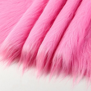 May include: A vibrant pink faux fur fabric featuring long, soft synthetic fibers. The material is arranged in deep, flowing folds that create a textured, layered appearance with varying light and shadow across the bright pink surface.
