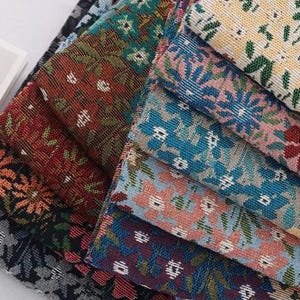 May include: A collection of folded fabric swatches featuring a dense, woven floral pattern. The textiles display a variety of colour combinations including deep red, teal, orange, black, light blue, pink, and cream, all with a textured finish.