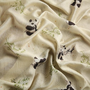 Pu&ograve; includere: Un tessuto color crema con un motivo ripetuto di panda bianchi e neri e steli di bamb&ugrave; verdi. Il materiale presenta una superficie sottilmente strutturata con pieghe e drappeggi visibili, che mettono in risalto le illustrazioni animali.