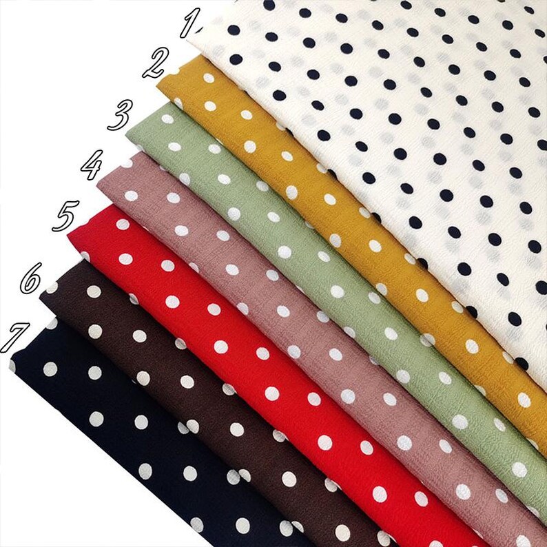 May include: Seven folded fabric swatches arranged in a stack, each featuring a polka dot pattern. The colors include white with black dots, mustard yellow, sage green, dusty rose, bright red, dark brown, and navy blue with white dots.