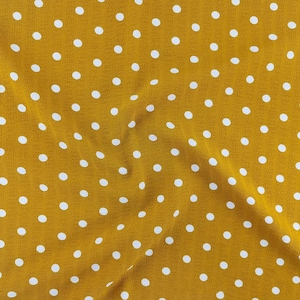 May include: A mustard yellow fabric featuring a repeating pattern of small, evenly spaced white polka dots. The material has a soft, slightly textured surface with gentle folds that create subtle shadows across the dotted design.