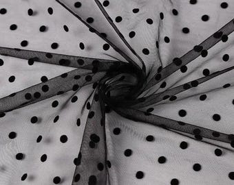 May include: Black sheer fabric with a polka dot pattern. The fabric is folded and draped, creating a swirling effect. The black dots are evenly spaced across the fabric, which appears to be lightweight and delicate.