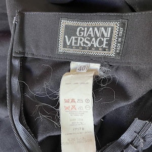 May include: Close-up of a black garment with a zipper and a label. The label reads "GIANNI VERSACE COUTURE" and "MADE IN ITALY". A size tag shows the number "40". The garment has care instructions and other text.
