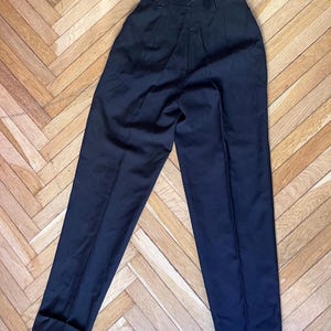 May include: Black trousers with a high waist and a tailored fit. The pants have a classic design with pleats at the front and cuffs at the hem. The dark color and simple style make them versatile for various outfits.