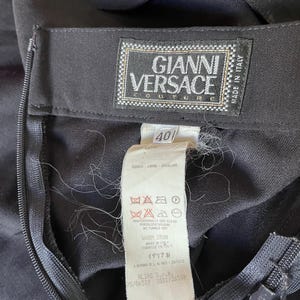 May include: Close-up of a black garment with a zipper and a Gianni Versace Couture label. The label includes the text "Made in Italy" and size 40. Additional care instructions are visible.