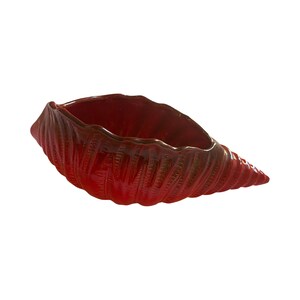 Puede incluir: Un macetero de cerámica roja en forma de concha de caracol. El macetero tiene un acabado brillante y una amplia abertura en la parte superior.