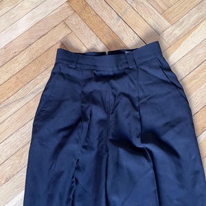 May include: A pair of navy blue high-waisted trousers with a tailored fit. The trousers feature a zipper closure, belt loops, and front pockets. The fabric has a slight sheen, and the pants are neatly pressed.