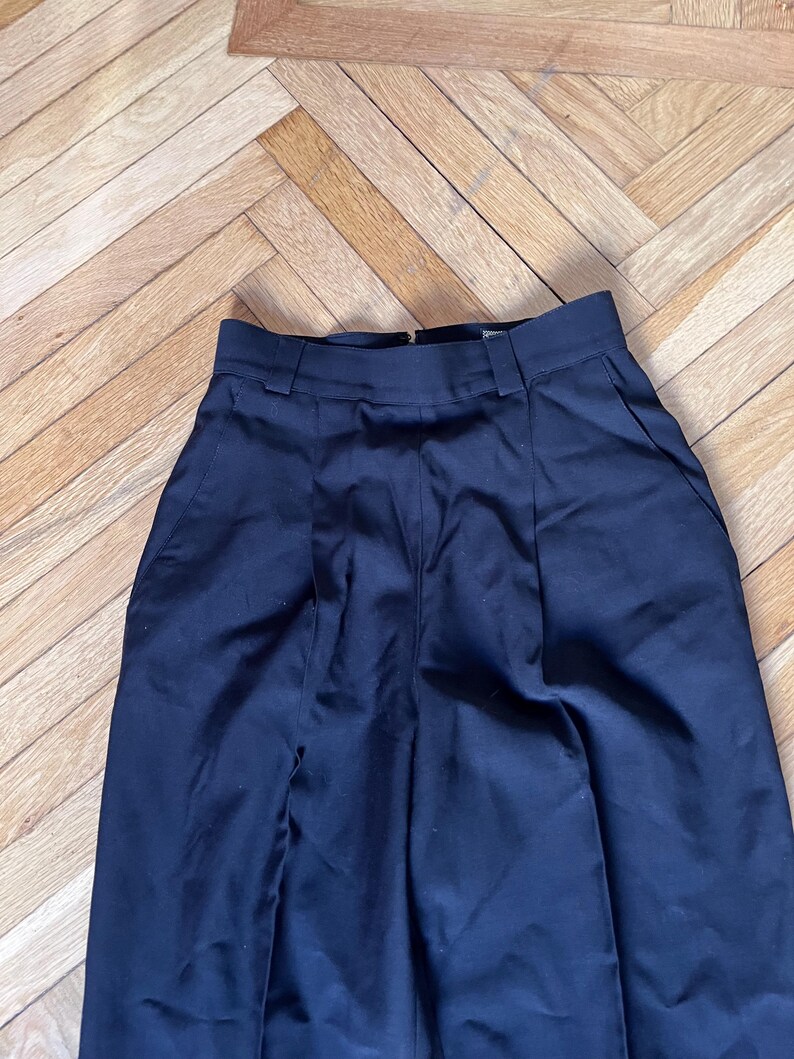 May include: A pair of navy blue high-waisted trousers with a tailored fit. The trousers feature a zipper closure, belt loops, and front pockets. The fabric has a slight sheen, and the pants are neatly pressed.