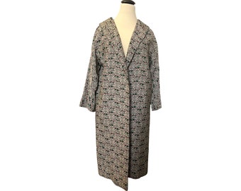 May include: A long, white coat with a floral print in shades of green, red, and black. The coat has a collar and a long, flowing silhouette.
