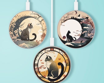 Op de afbeelding: Drie ronde draadloze opladers met kattenillustraties. Elke oplader heeft een ander kattenontwerp tegen een achtergrond van Japans geïnspireerde landschappen met kersenbloesems, pagodes en manen. De opladers hebben witte oplaadkabels.
