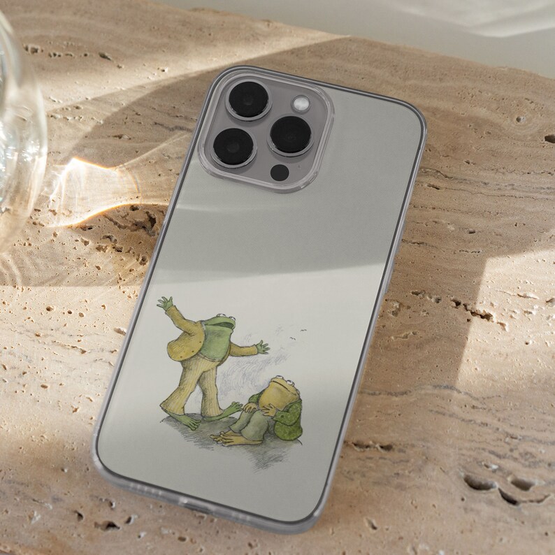iPhone 15 Pro Max 14 Plus 13 12 11 clear case with Frog and Toad Aesthetic design on it, there are total of five phone cover options to choose from. Green cottage core, nature core, old children book, animals, pastel cover artworks are depcited.