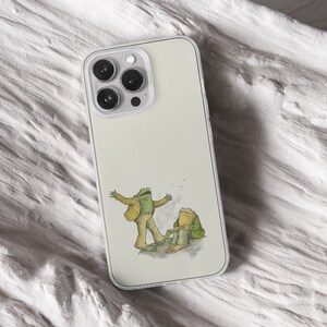 iPhone 15 Pro Max 14 Plus 13 12 11 clear case with Frog and Toad Aesthetic design on it, there are total of five phone cover options to choose from. Green cottage core, nature core, old children book, animals, pastel cover artworks are depcited.