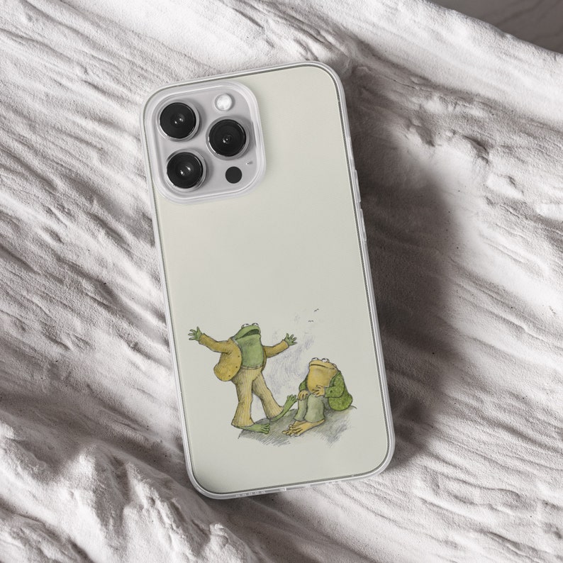 iPhone 15 Pro Max 14 Plus 13 12 11 clear case with Frog and Toad Aesthetic design on it, there are total of five phone cover options to choose from. Green cottage core, nature core, old children book, animals, pastel cover artworks are depcited.