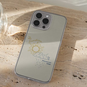May include: A clear phone case with a light gray background and a design of a sun with a yellow center and a blue cloud with rain drops. The text "He was sunshine, I was midnight rain" is printed on the case.