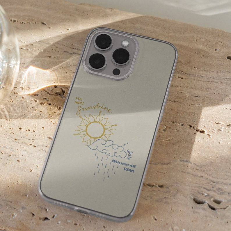 May include: A clear phone case with a light gray background and a design of a sun with a yellow center and a blue cloud with rain drops. The text "He was sunshine, I was midnight rain" is printed on the case.