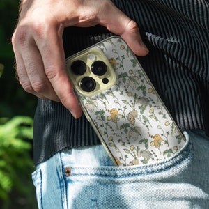 May include: A clear phone case with a white background and a pattern of small yellow and brown animals. The case has a camera lens cutout and a white border.