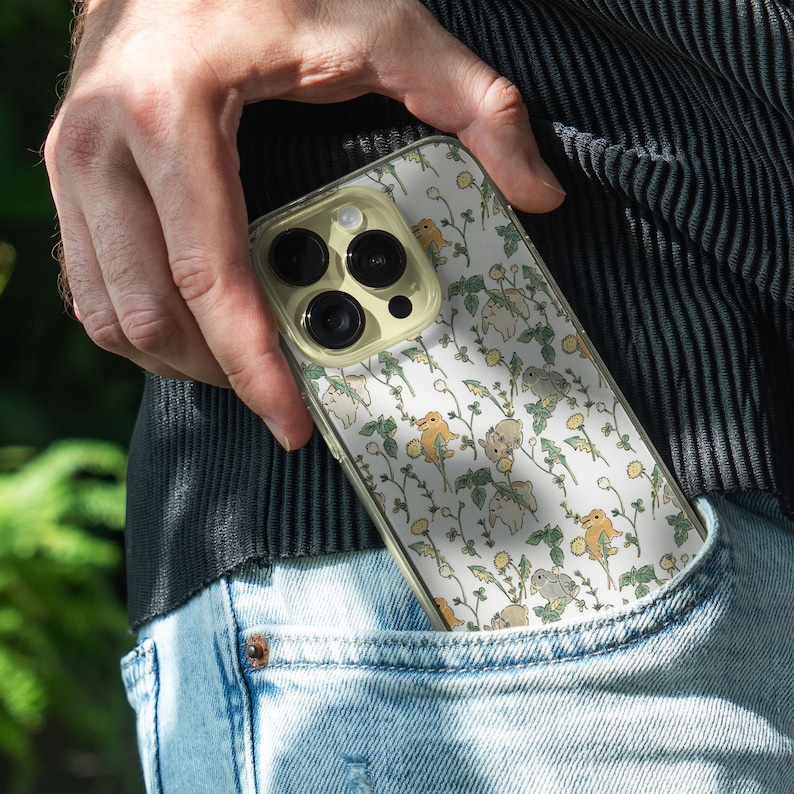 May include: A clear phone case with a white background and a pattern of small yellow and brown animals. The case has a camera lens cutout and a white border.