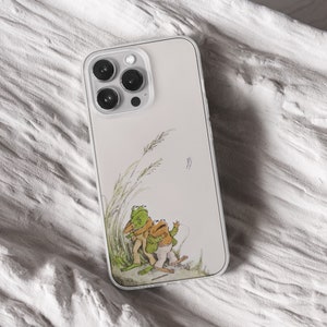 iPhone 15 Pro Max 14 Plus 13 12 11 clear case with Frog and Toad Aesthetic design on it, there are total of five phone cover options to choose from. Green cottage core, nature core, old children book, animals, pastel cover artworks are depcited.