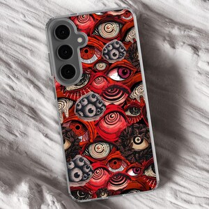 Puede incluir: Una funda transparente para tel&eacute;fono con un patr&oacute;n de ojos rojo, blanco y negro. La funda tiene una protuberancia de c&aacute;mara elevada con tres lentes.