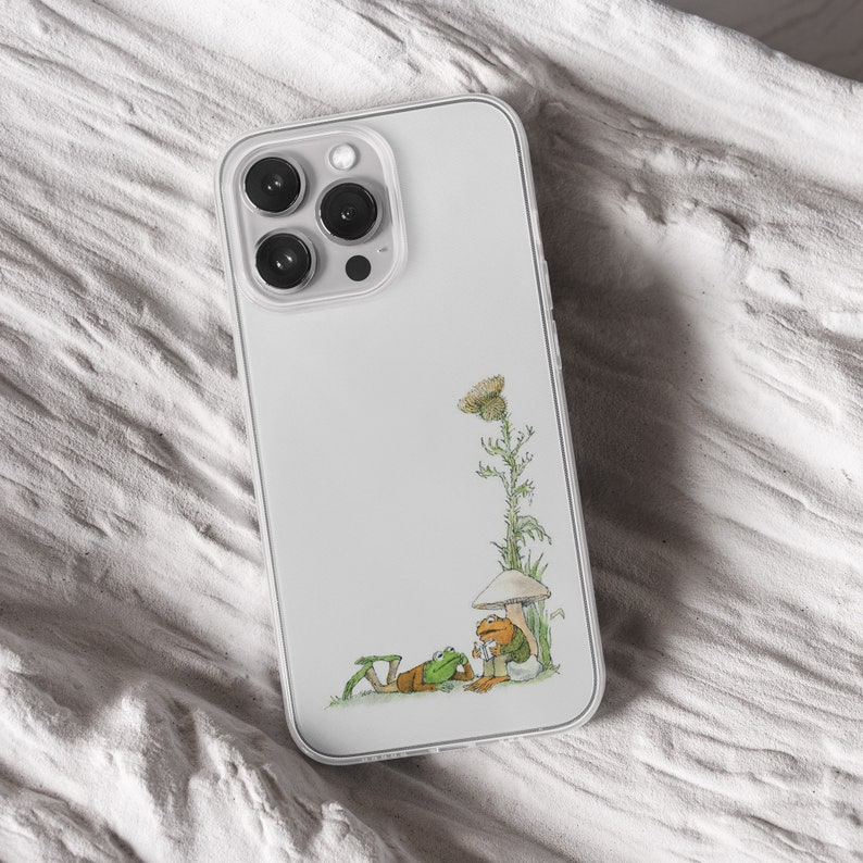 iPhone 15 Pro Max 14 Plus 13 12 11 clear case with Frog and Toad Aesthetic design on it, there are total of five phone cover options to choose from. Green cottage core, nature core, old children book, animals, pastel cover artworks are depcited.