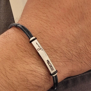 May include: A black braided bracelet with a silver rectangular charm engraved with the date "02.02.2014" and a small infinity symbol.