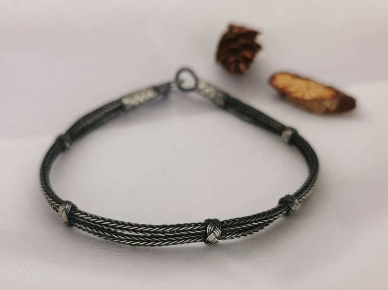 May include: A silver bracelet with a braided design and four knots. The bracelet is made of two strands of silver wire that are braided together.