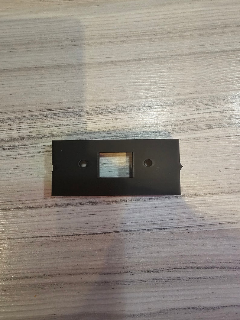 May include: A black plastic wall plate with a rectangular cutout and two small holes.