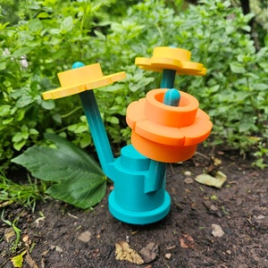 May include: A teal blue, 3D printed, flower-shaped object with orange and yellow petals. The object has a stem and two yellow flower-shaped tops.
