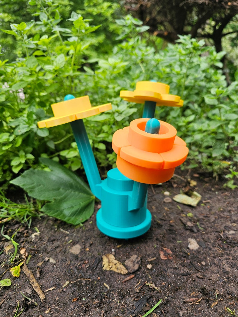 May include: A teal blue, 3D printed, flower-shaped object with orange and yellow petals. The object has a stem and two yellow flower-shaped tops.