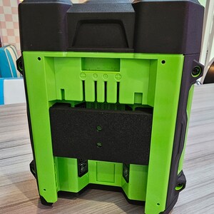 May include: A black and green portable speaker with a black foam cover over the speaker grille. The speaker has a black plastic handle on the top and a black plastic base. The speaker has a series of buttons on the back, including a power button, a volume button, and a play/pause button.