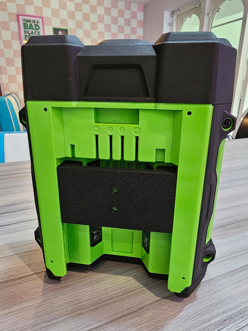 May include: A black and green portable speaker with a black foam cover over the speaker grille. The speaker has a black plastic handle on the top and a black plastic base. The speaker has a series of buttons on the back, including a power button, a volume button, and a play/pause button.